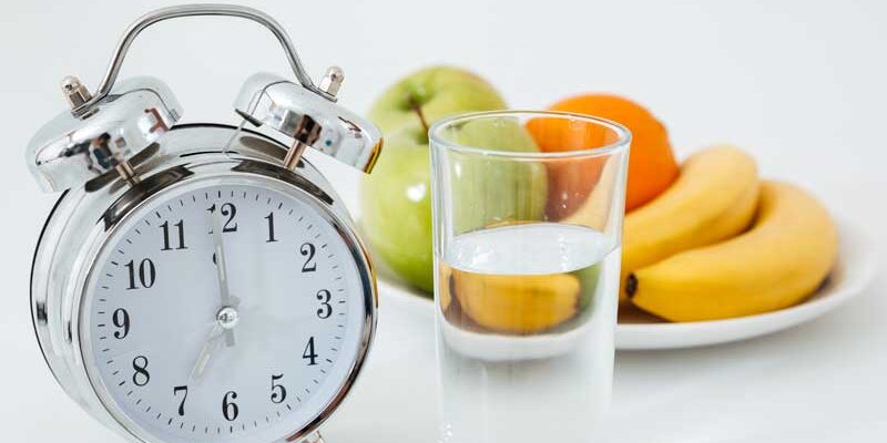 sveglia, frutta e un bicchiere di acqua simbolo di digiuno