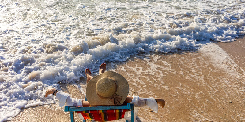 Mujer relajada en una tumbona en la playa observando las olas.