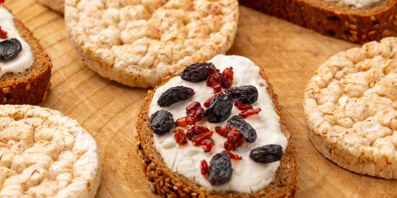 Fetta di pane integrale con ricotta, frutti rossi e frutta secca, affiancata da alcune gallette di riso.