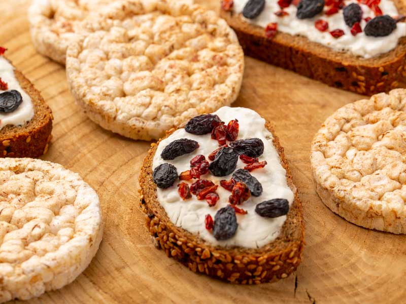 Fetta di pane integrale con ricotta, frutti rossi e frutta secca, affiancata da alcune gallette di riso.